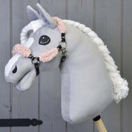 Zwart halster met Old Rose bont compleet - kunstleer van Hobby Horse LarDen op een pluche hobby horse met een lichtgrijs hoofd, witte gevlochten manen en zwart halster, gemonteerd op een houten stok tegen een achtergrond van houten panelen.