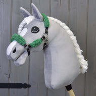 Een grijze pluche hobby horse van Hobby Horse LarDen met een zwart kunstleren halster met volledig groen bont, tegen een achtergrond van houten panelen.