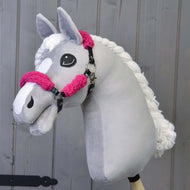 Hobby Horse LarDen met een handgemaakte grijze hobby horse met witte manen en gezichtsaftekening, die het Zwart halster met compleet roze bont - kunstleer draagt, getoond tegen een houten achtergrond.