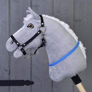 Hobby Horse cordeo blauw (maat S) van Hobby Horse LarDen op een grijs pluchen lichaam met witte manen, zwart hoofdstel en blauw-violet lint op een houten stok, weergegeven tegen een grijze houten wand.