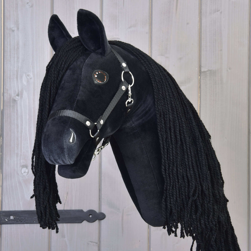 Black hobby horse with long black yarn mane and bridle, mounted on a wooden background with a dark metal hinge.