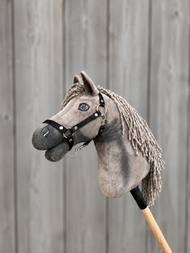Hobby Horse Swing met Zwart Halster - maat S van Hobby Horse LarDen, met een grijze Hobby Horse met een zwart halster en manen van garen, gemonteerd op een houten stok, tegen een achtergrond van grijze houten planken.