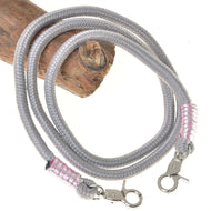 The Reins Tizian by Hobby Horse LarDen feature coiled gray polypropylene with silver lobster clasps and pink-silver wraps at each end, shown on wood against a white background—ideal as stylish handmade or hobby horse reins.
