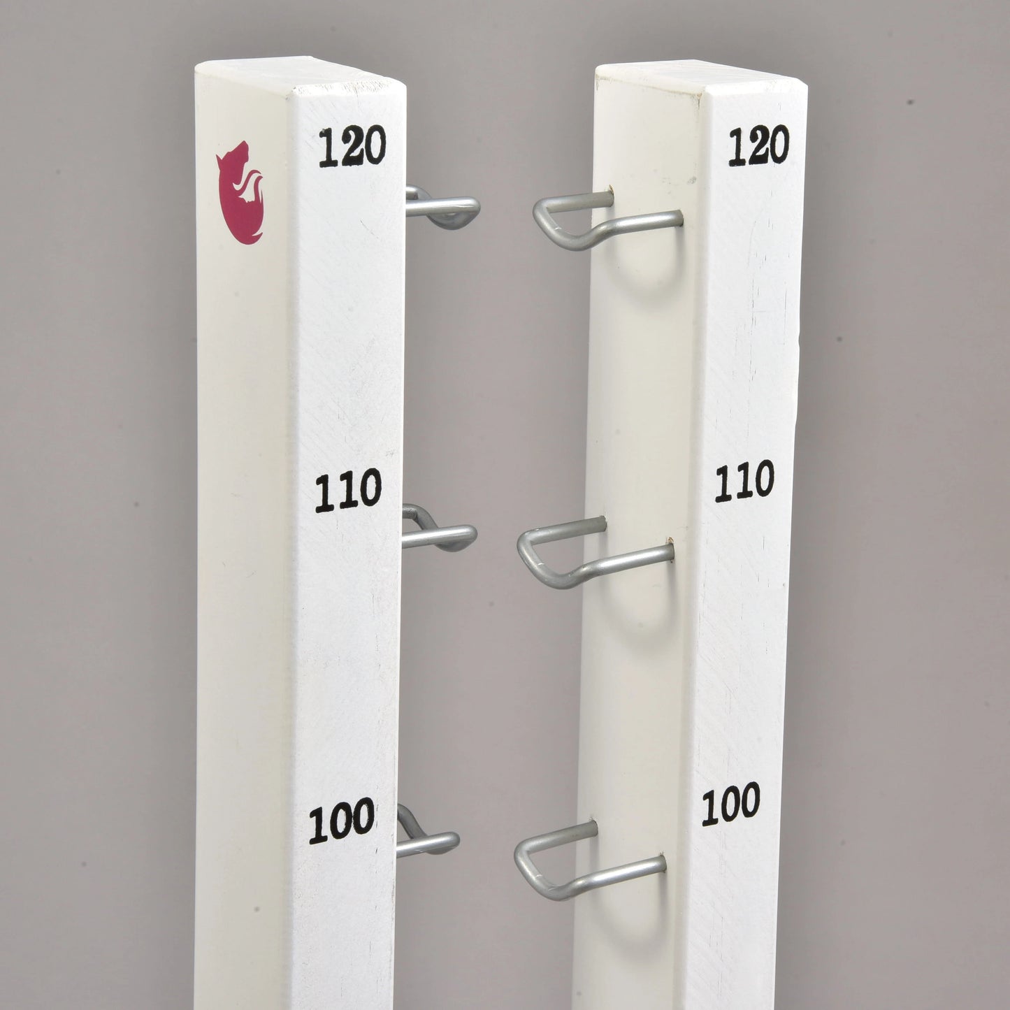 The Jump set for Hobby Horsing by Hobby Horse LarDen features two white vertical posts with metal brackets at 100, 110, and 120 heights, ideal for jumps or cavaletti. The left post is topped with a red fox logo. Background is plain gray.