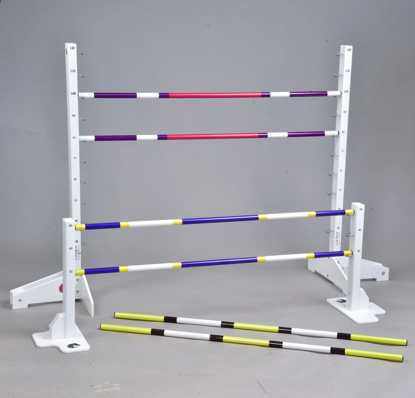 The Hobby Horse LarDen Jump Set for Hobby Horsing includes white adjustable jumps and colorful poles, arranged at varying heights or on the ground, ideal for equestrian-style, cavaletti, or dog agility training.
