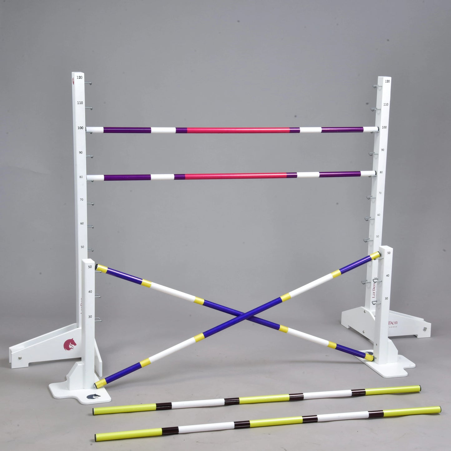 The Hobby Horse LarDen Jump set for Hobby Horsing includes white standards with measuring marks, four colored poles (two horizontal and two crossed), and two yellow-and-black cavaletti in front, shown against a plain gray background.