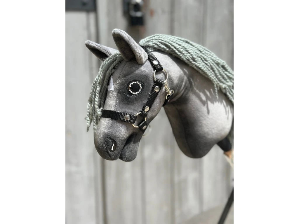A close-up of the Hobby Horse LarDen "Little Prince" (size XS), featuring a grey fabric head, black halter, button eyes, and yarn mane against a blurred wooden background.