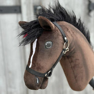 A close-up of Hobby Horse LarDen's "Hobby Horse Lucas with Black Halter," a brown Hannoverian stallion with a black mane, white facial stripe, and black halter, set against a blurred wooden background.