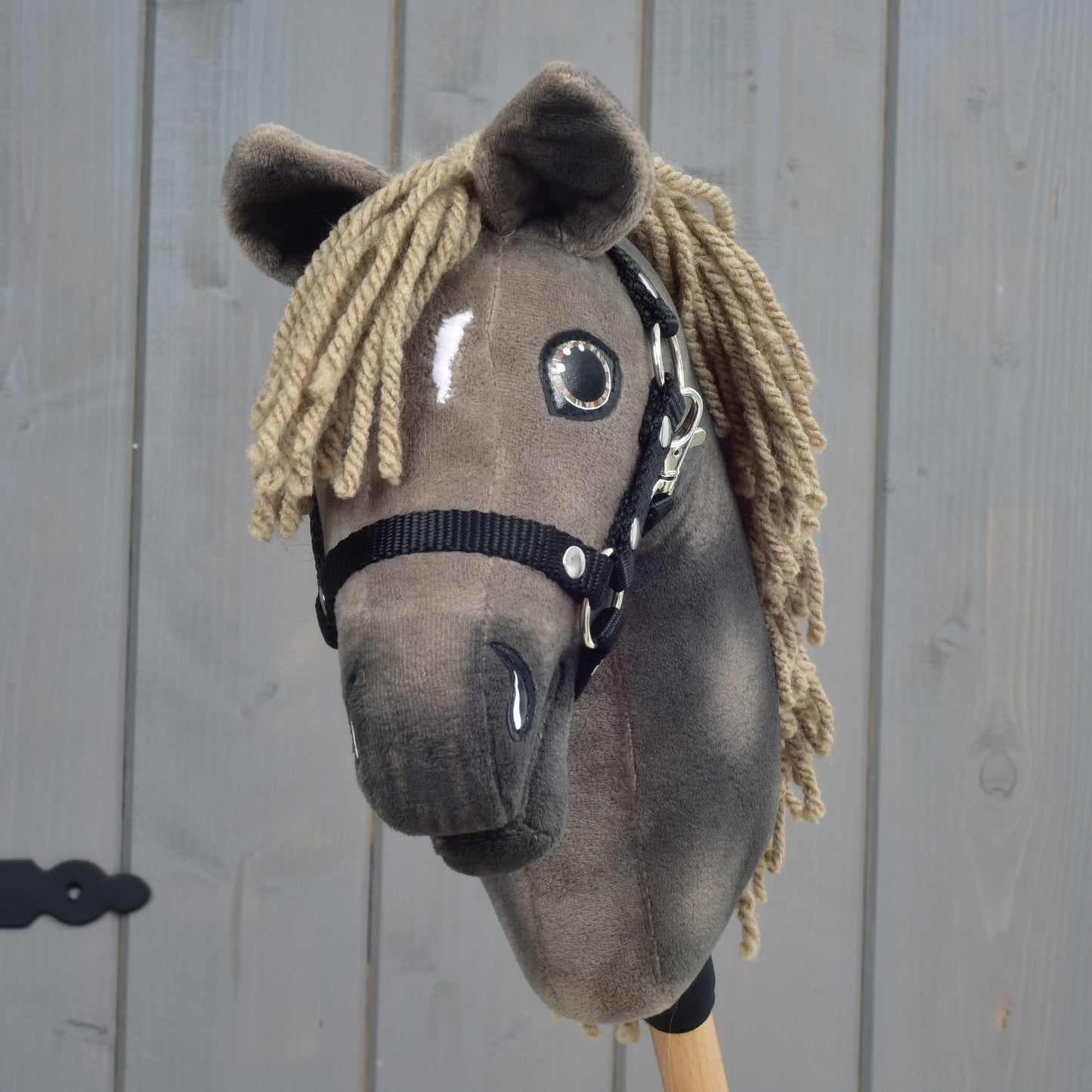Hobby Horse LarDen Avalon, maat XS, met een bruine pluchen kop, zwart halster en manen van garen, geïnspireerd op een Engelse Warmbloed sportpaard, weergegeven tegen een houten achtergrond.