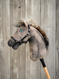 Close-up van Hobby Horse Bolero met zwart halster - maat S van Hobby Horse LarDen, met een bruin Appaloosa-ontwerp, blauw oog, pluizige manen en een achtergrond van houten planken.