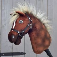 Close-up van Hobby Horse Cinnamon met zwart halster - maat S van Hobby Horse LarDen, met een bruin pluchen lichaam, een pluizige manen en een zwart halster, die doet denken aan een trotse hengst, tegen een houten achtergrond.