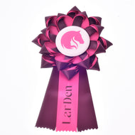 A pink and burgundy dressage ribbon called "Hobby Horse Ribbon Raspberry Rose" from Hobby Horse LarDen, featuring a horse head silhouette in the center and "LarDen" written on one of the tails.