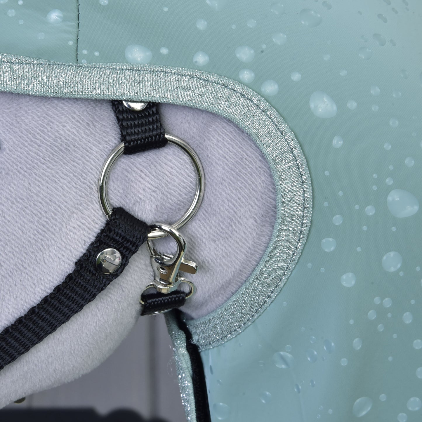 Close-up van een paard dat Regenjas Greeny van Hobby Horse LarDen draagt, met een metalen ring, zwarte riem, clip en zachte lichte voering met druppels, voor all-weather bescherming.