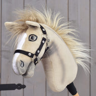 Hobby Horse Ivory Dream met zwart halster van Hobby Horse LarDen, maat XS, vastgehouden door een persoon, met een lichtbruine vacht, witte aftekeningen op het gezicht, een pluizige manen en een zwart halster, tegen een houten achtergrond.