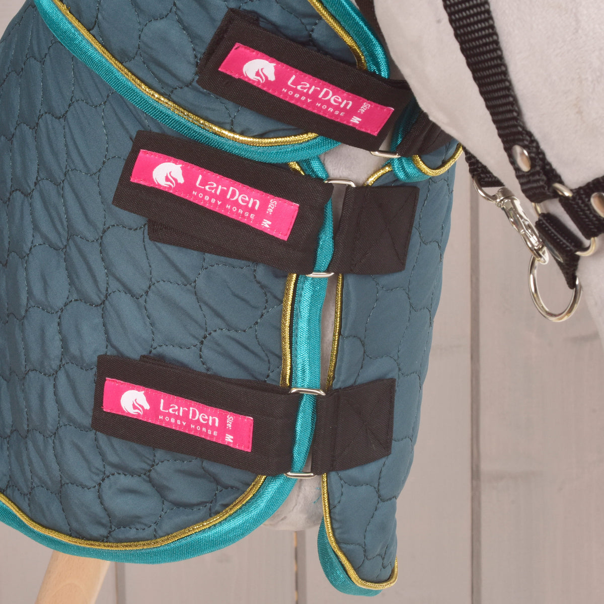 Detail of three black fastening straps on the green quilted blanket worn by a Hobby Horse