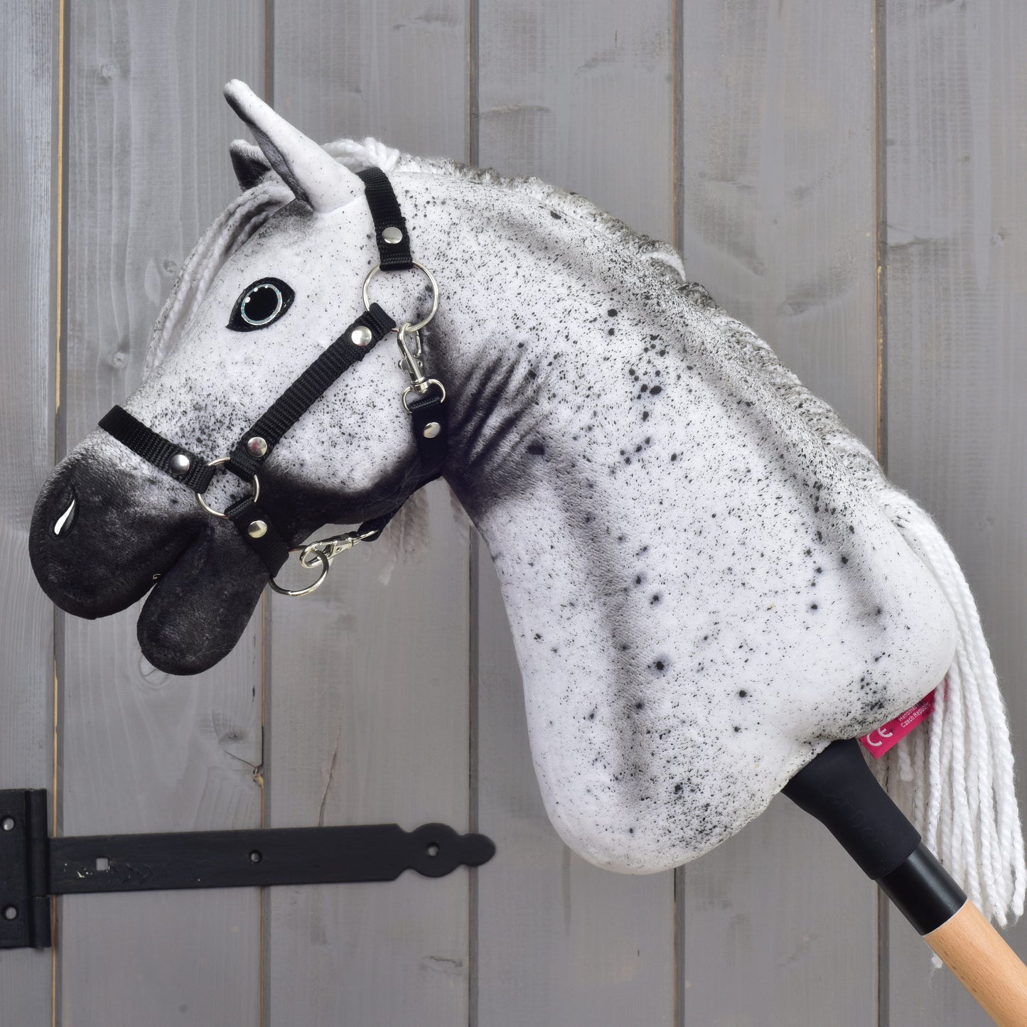 Hobby Horse Naivy met zwart halster - maat S van Hobby Horse LarDen, met een realistische grijze en zwarte hengstenkop en een zwart halster, getoond voor een grijze houten wand.