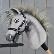 Hobby Horse Prestige met zwart halster, maat XS van Hobby Horse LarDen, met een grijs pluchen ontwerp, een stekelige manen en een zwart halster, geïnspireerd op de elegantie van een Engelse warmbloed. Het is gemonteerd op een houten stok en getoond tegen een achtergrond van houten panelen.