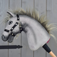 Hobby Horse Prestige met zwart halster, maat XS van Hobby Horse LarDen is een grijze pluchen Hobby Horse-kop, geïnspireerd op de elegantie van een Engelse warmbloed-sportpaard. Het heeft een expressief geborduurd gezicht, een wilde manen en een stevig zwart halster, gemonteerd op een houten stok. Geposeerd tegen een houten achtergrond, ideaal voor fantasierijke springavonturen.