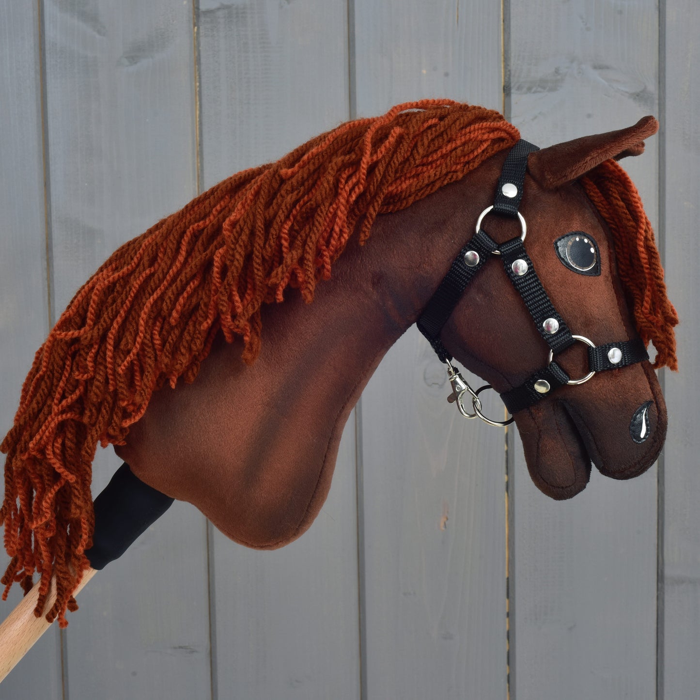 The Hobby Horse LarDen "Hobby Horse Rebel with Black Halter" in size XS, featuring a brown Hanoverian design with a thick orange-brown yarn mane, black bridle and reins, is displayed against a wooden plank background.