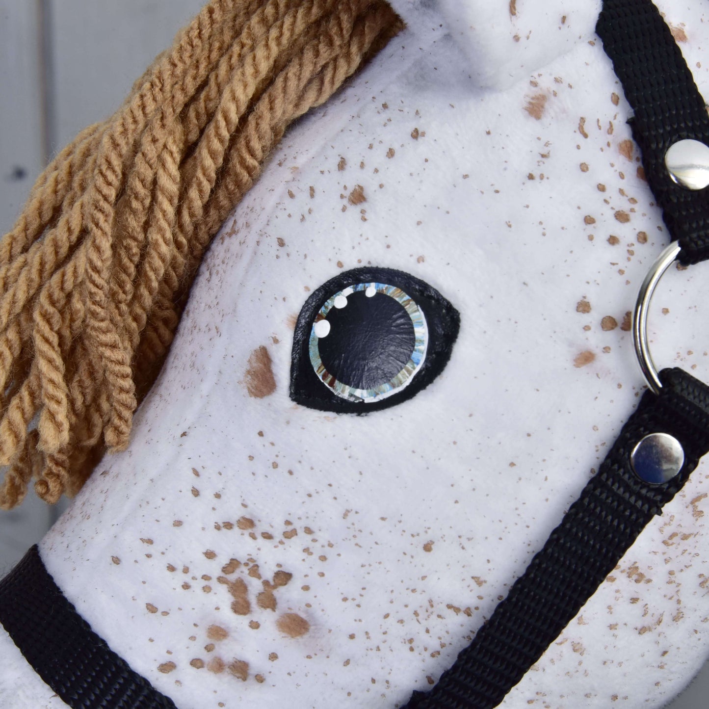 Close-up van "Rufus with Black Halter" van Hobby Horse LarDen: een wit Appaloosa Hobby Horse met bruine manen van garen, zwart halster, gestikt zwart-wit oog en pluchen stof met bruine vlekken zoals een Appaloosa-hengst.