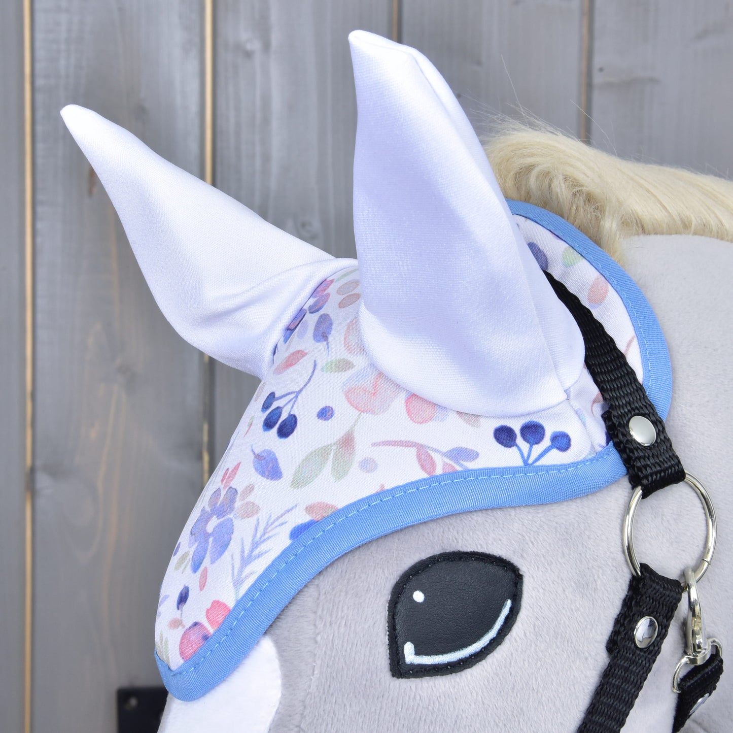 Close-up van Set Vanessa NEW van Hobby Horse LarDen: een pluchen hobby horse-hoofd met een pastelkleurig bloemig oornetje met zachte witte oren, getoond tegen een houten achtergrond.