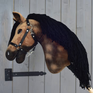 Hobby Horse Stormy met zwart halster van Hobby Horse LarDen, bruin pluche met zwarte garenmanen, gemonteerd op een metalen beugel tegen een houten wand.