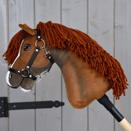 Hobby Horse Cooper met zwart halster van Hobby Horse LarDen met een bruine stoffen kop met manen van garen, een witte bles op de neus en gemonteerd op een houten stok. Gestyled als een elegant sportpaard, ideaal als fantasierijke dressuuravonturen en hier gefotografeerd tegen een grijze houten achtergrond.