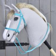 Grijze pluche Hobby Horse met lichte manen, met het Hobby Horse LarDen Zwart hoofdstel met teugels van turquoise band, gemonteerd op een houten stok en geplaatst voor een grijs houten hek.