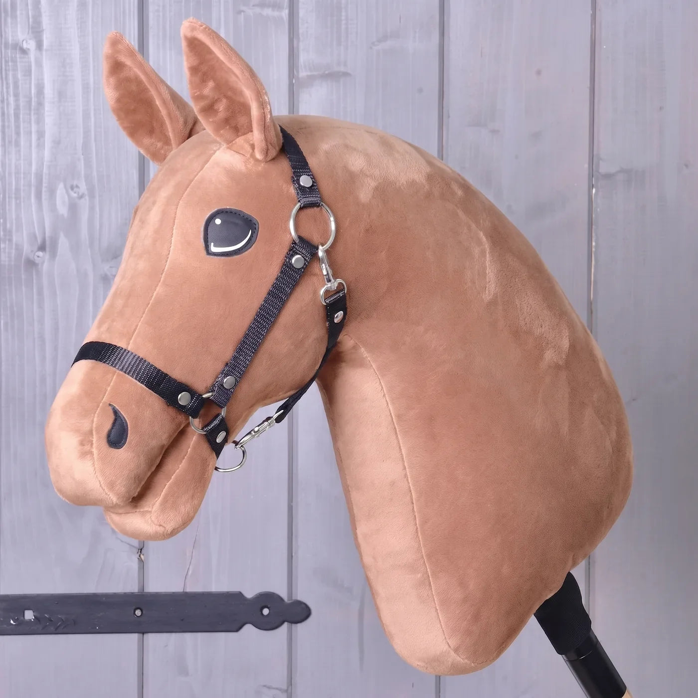Bouw je paard van Hobby Horse LarDen — een pluchen Hobby Horse-hoofd met een hoofdstel, gemonteerd op een stok, tegen een houten wandachtergrond, ideaal als inspiratie om je eigen unieke paard te maken met de configurator “Build your horse” van Hobby Horse LarDen voordat je je aankoop afrondt.