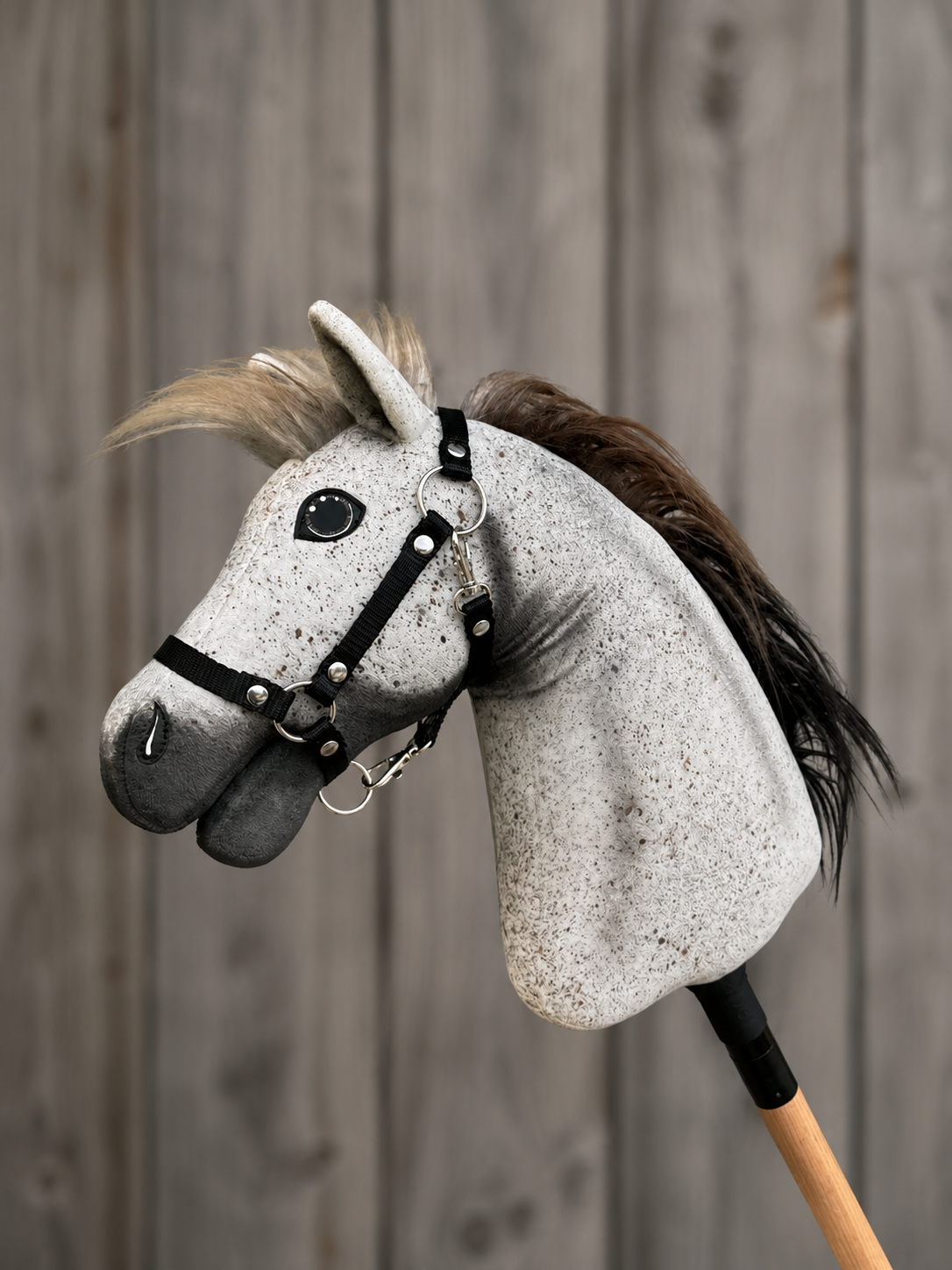 The Hobby Horse LarDen Luna with Black Halter (size S) features a lively design with a black-and-brown mane, mounted on a wooden stick, and is set against rustic wooden planks.