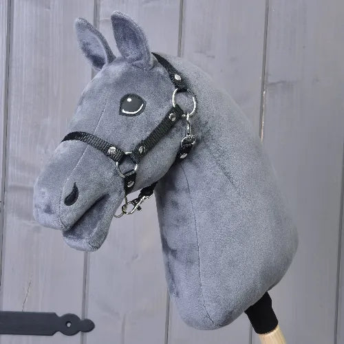 Bouw je paard van related_to_12441055625556, een Hobby Horse met een donkergrijze vacht met subtiele blesaftekeningen en een zwart hoofdstel, gemonteerd op een houten stok en getoond tegen een grijze houten wand.