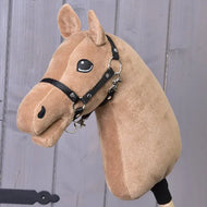A plush "Build your horse" hobby horse head by related_to_12441055625556, featuring a brown coat with caramel accents, dark grey mane, black bridle, and friendly embroidered eyes, showcased against a wooden wall background.