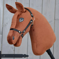 Bouw je paard, aanpasbaar Hobby Horse met een donker kastanjebruine pluche kop, een zwart halster en een opvallende bruin-witte manen, gemonteerd op een stok tegen een grijze houten achtergrond