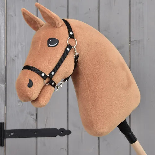 Bouw je paard van related_to_12441055625556, een handgemaakt voskleurig Hobby Horse-hoofd met een zwart tuig op een stok, met opgenaaide ogen en neusgaten, afgebeeld tegen een grijze houten achtergrond.