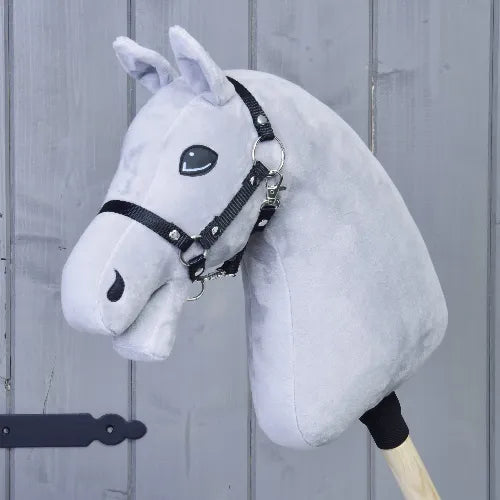 Lichtgrijs Bouw je paard Hobby Horse van related_to_12441055625556 met opvallende blauwe ogen en een zwart hoofdstel, gemaakt van pluche materiaal en gemonteerd op een houten stok, geplaatst voor een verticale houten wand.