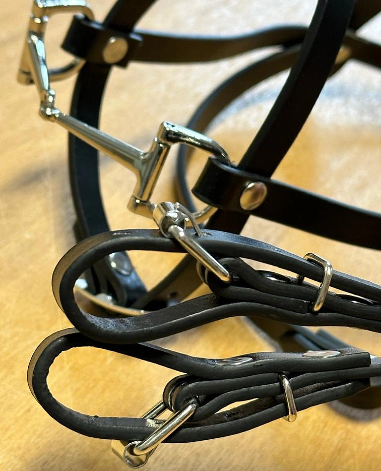Close-up van een zwart leren paardenhoofdstel en teugels met glanzende zilverkleurige metalen gespen en ringen, perfect voor een Hobby Horsing-uitrusting, liggend op een lichtbruin oppervlak.