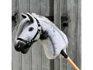 The Hobby Horse LarDen "Naivy" with a black halter is displayed in front of a rustic wooden door, showing off its gray and white Appaloosa styling and detailed mane.