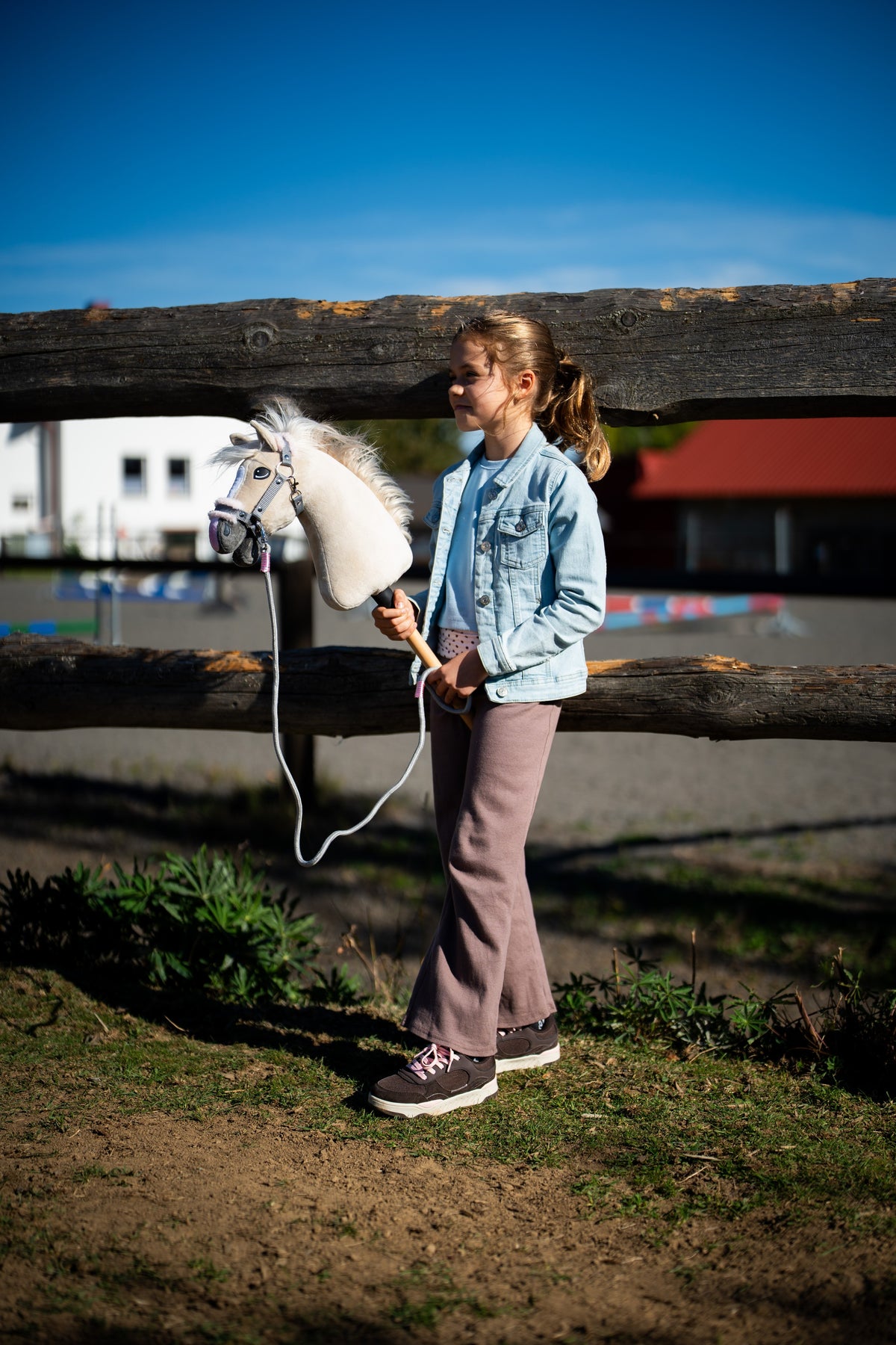 Young girl in a denim jacket at a log fence holding Hobby Horse Pixie in a grey fur halter with a lead rope