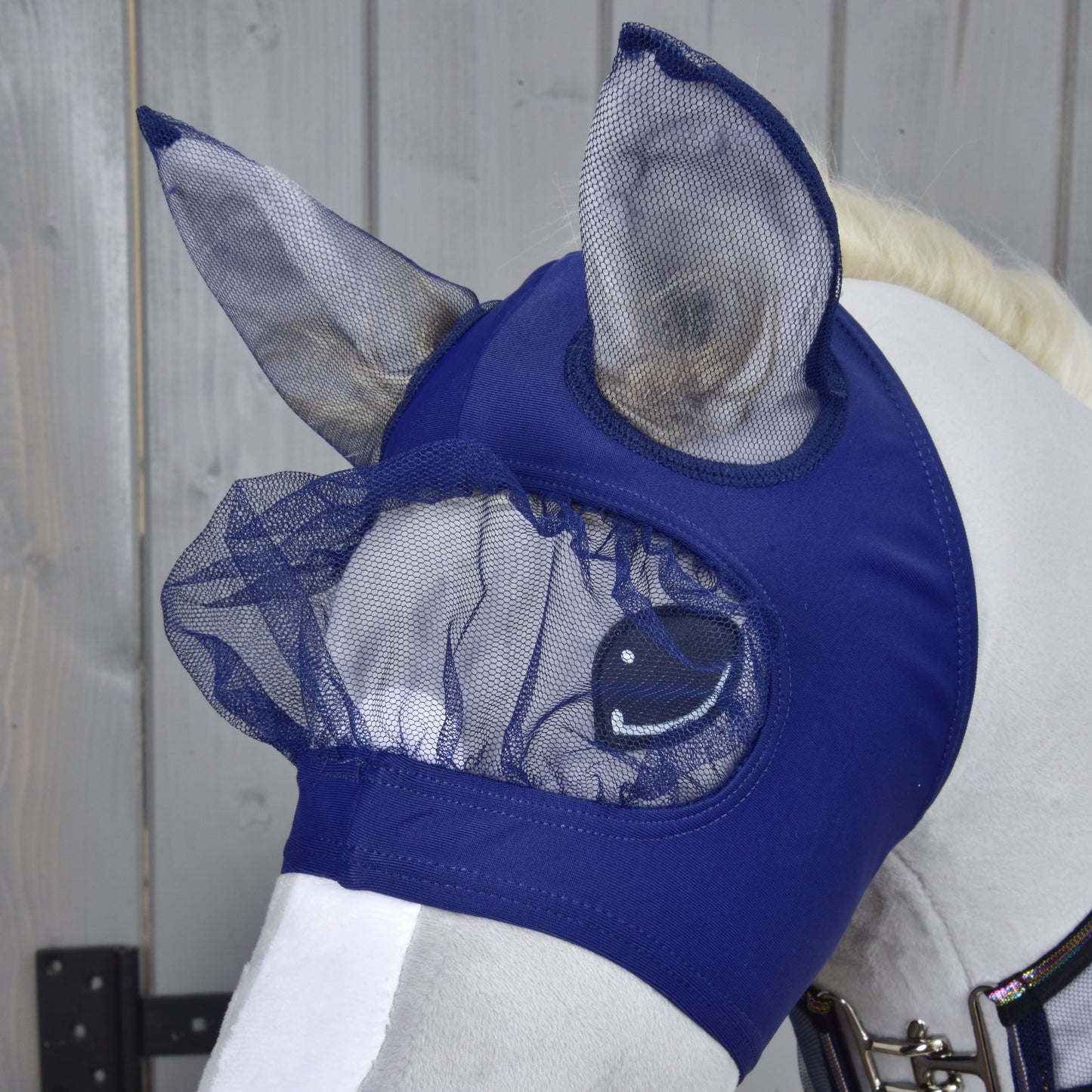Een wit paard draagt de Hobby Horse LarDen Set Vlieg Combo in marineblauw, met mesh oor- en oogbescherming. Perfect voor Hobby Horsing-stijl, dit masker beschermt de ogen en oren van je paard tegen insecten.