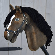 Hobby Horse Sundance met zwart halster van Hobby Horse LarDen met een bruine kop, geïnspireerd op de snelheid van hengsten, met een zwarte manen van garen, witte bles en zwart halster, gemonteerd op een stevige houten stok voor een grijze houten wand.